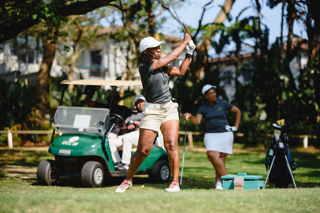 A golfer following through on a swing beside a golf cart